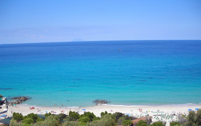 Spiaggia con sabbia bianca e mare azzurro, vegetazione sullo sfondo.