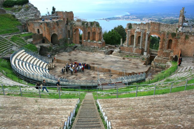 Antico teatro in pietra con gradinate semicircolari, vista mare.