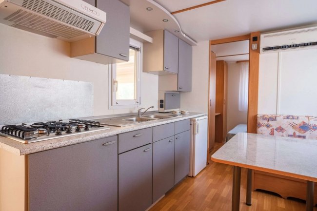 Cucina moderna con piano cottura, lavello, armadietti grigi e tavolo.