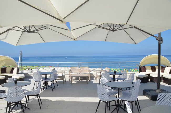 Una terrazza con sedie bianche e grandi ombrelloni bianchi vista mare.
