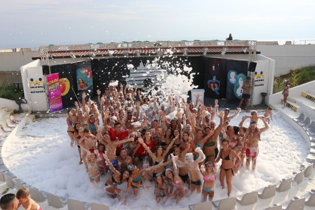 Una festa in piscina piena di schiuma con molte persone in costume.