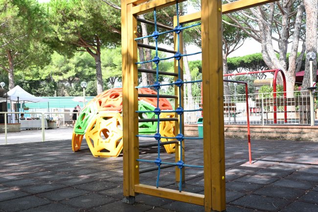 Struttura da arrampicata in legno e corda, con giochi colorati sullo sfondo.