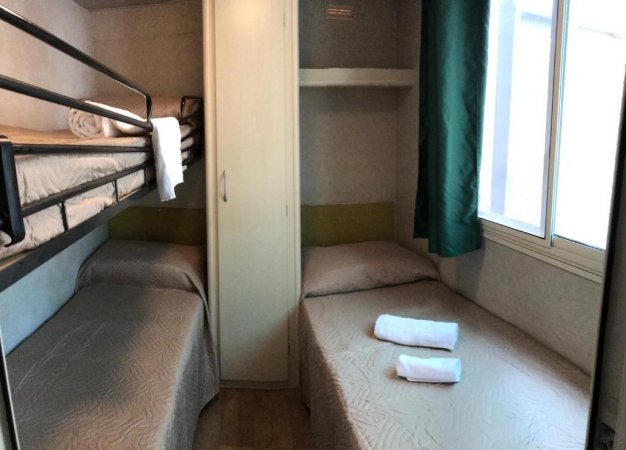 Stanza con letto a castello, letto singolo, armadio e finestra con tenda verde.