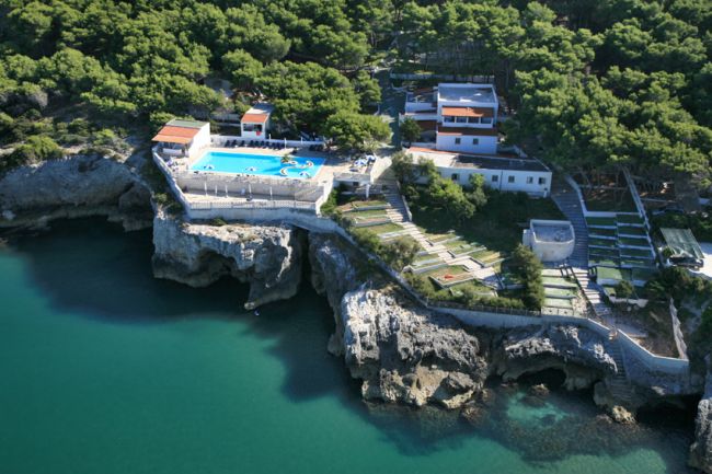 Vista aerea di un complesso con piscina su una scogliera, circondato da alberi verdi vicino al mare.