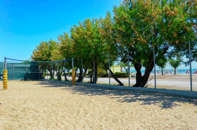 Campo da beach volley con rete, alberi e vista sul mare.