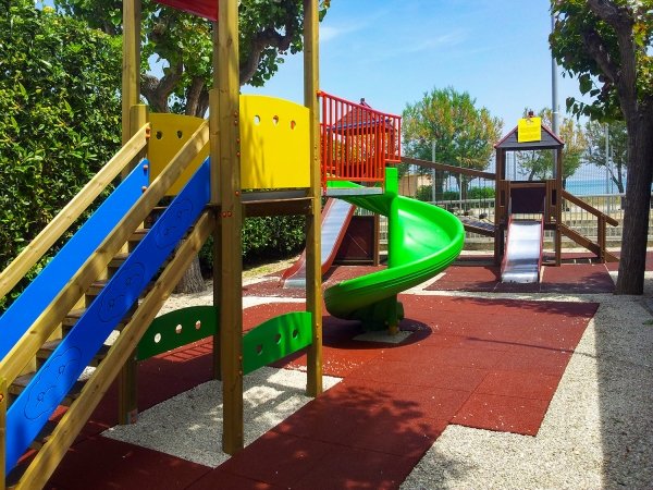 Parco giochi con scivoli colorati e pavimentazione in gomma rossa.