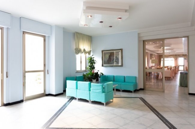 Area salotto con divani turchesi e piante verdi.