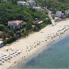 Una spiaggia affollata con una villa immersa nel verde sulla collina.