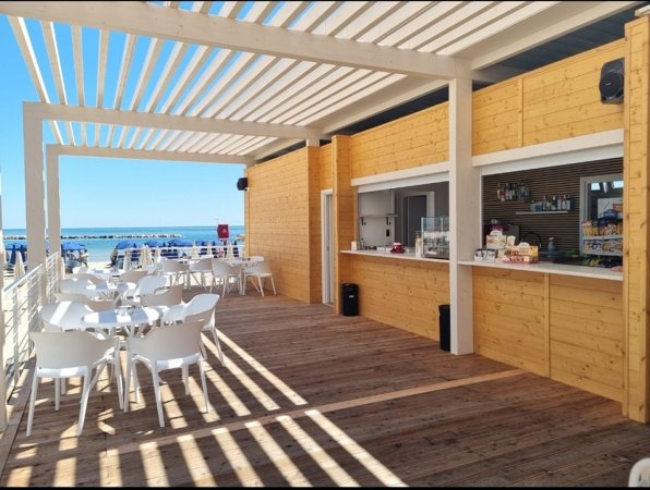 Terrazza vista mare con sedie e tavoli bianchi.