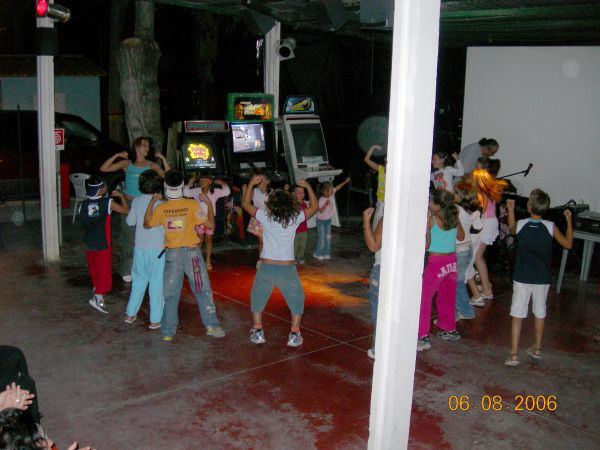 Bambini che ballano in una sala con videogiochi e luci soffuse.