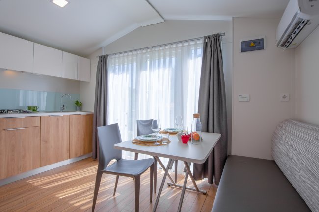 Cucina moderna con tavolo apparecchiato, tende leggere e mobili in legno chiaro.