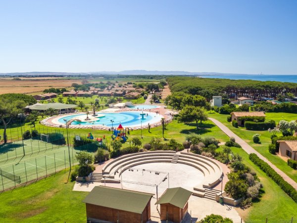 Panorama di un villaggio turistico con piscina, campi da tennis e mare.
