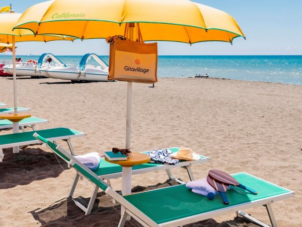 Spiaggia con ombrelloni gialli, lettini verdi e mare sullo sfondo.