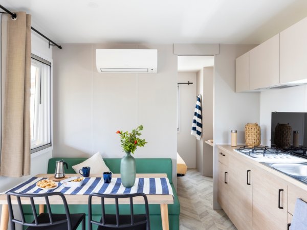 Interno moderno con tavolo apparecchiato, divano verde e cucina attrezzata.