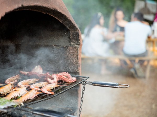 Cibo, tra cui gamberi e polpo, griglia su barbecue con persone sedute sullo sfondo.