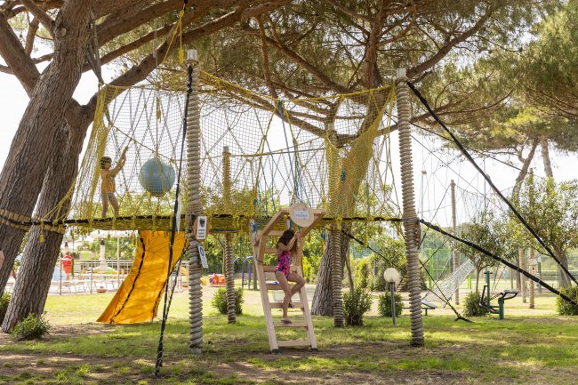 Bambini giocano su struttura sospesa con scivolo.
