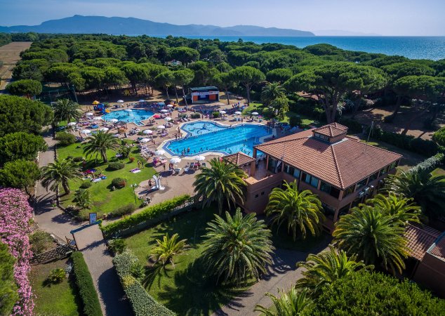 Complesso con piscine, palme e strutture con tetti rossi vicino alla costa.