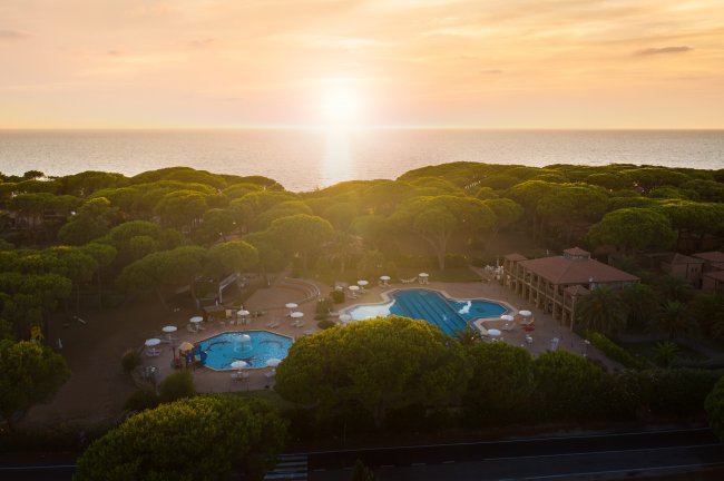 Tramonto su un complesso con piscine e alberi vista mare.
