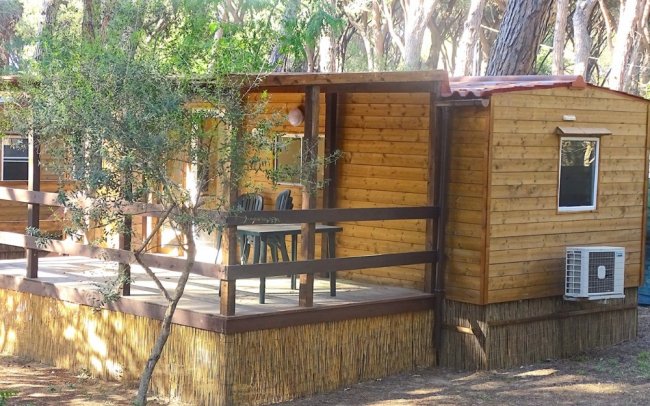 Casetta in legno semplice con veranda, sedie e tavolo esterni.