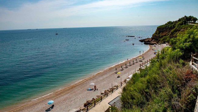 Spiaggia di ciottoli con ombrelloni e scogli.