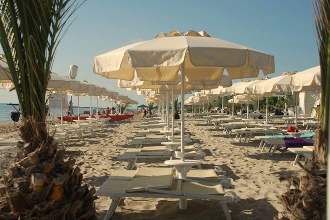 Spiaggia sabbiosa con lettini e ombrelloni bianchi.