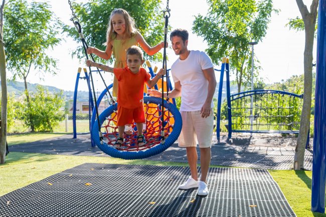Due bambini su un'altalena a nido con un adulto in un parco giochi.