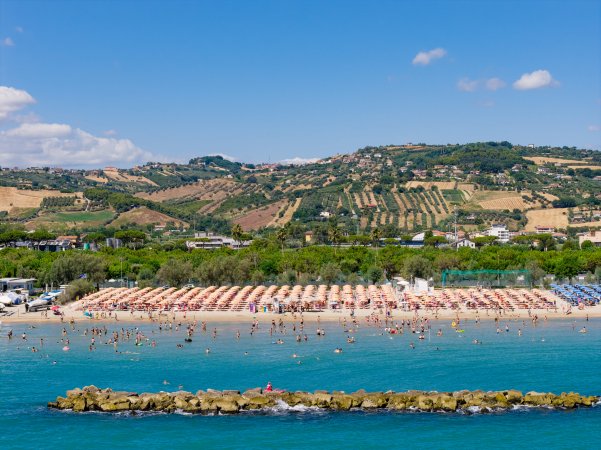 Spiaggia con ombrelloni, mare e colline sullo sfondo.