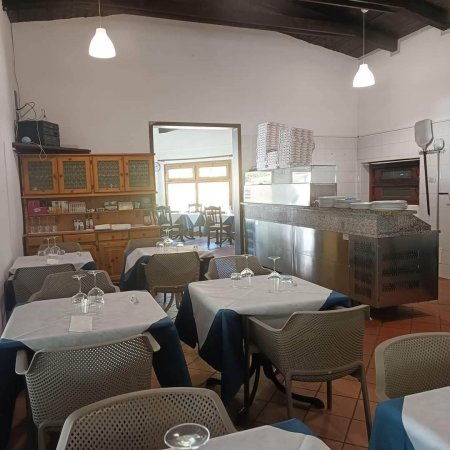 Interno di ristorante con tavoli apparecchiati e un banco da cucina.