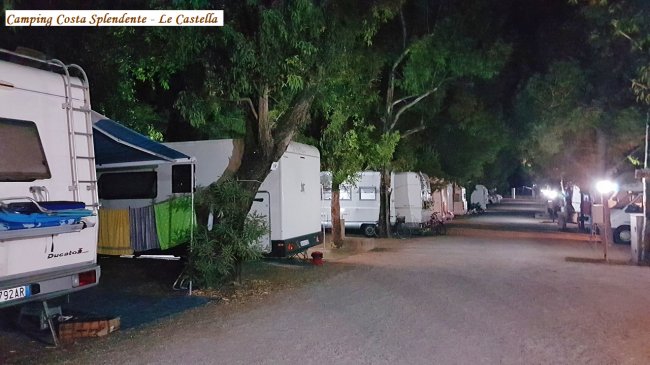 Viale di un campeggio di notte, illuminato e fiancheggiato da camper.