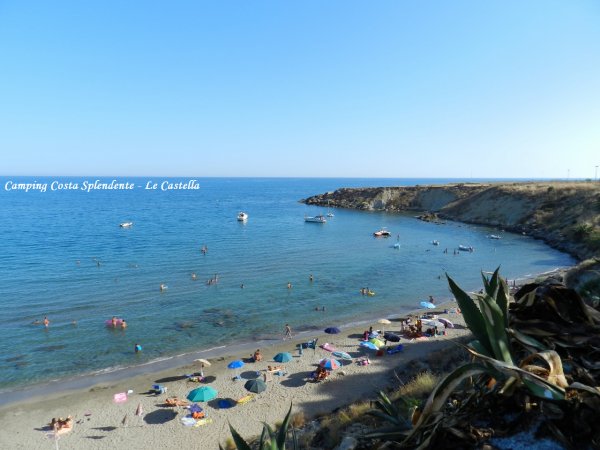 Spiaggia con ombrelloni colorati, persone in acqua e barche lontane.