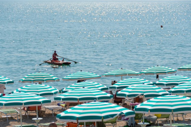Spiaggia con ombrelloni verdi e bianchi, barca a remi in mare.