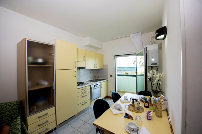 Cucina moderna con mobili gialli, tavolo apparecchiato e vista mare dalla finestra.