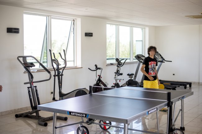 Sala fitness con attrezzature e tavolo da ping pong, persona in piedi.