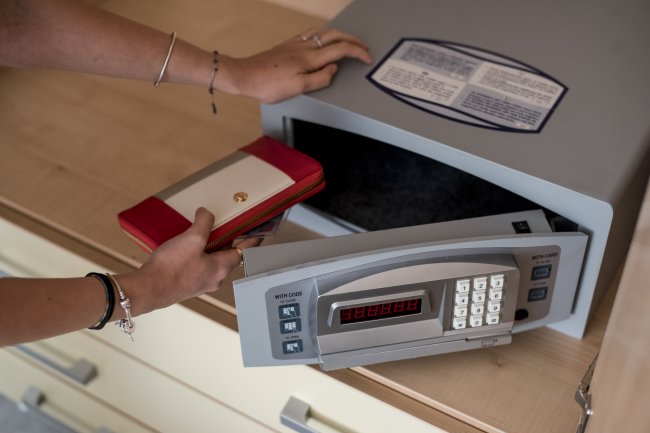 Una persona ripone un portafoglio rosso e bianco in una cassaforte elettronica aperta.