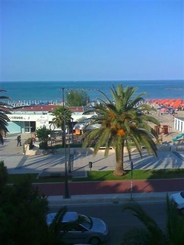 Spiaggia con palme, cabine, ombrelloni arancioni e mare azzurro sullo sfondo.