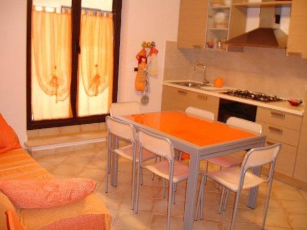 Cucina con tavolo arancione, sedie bianche, divano arancione e mobili chiari.