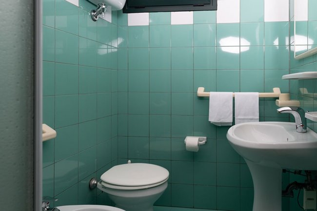 Bagno con piastrelle verdi, wc e lavandino.