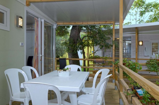 Terrazza con tavolo bianco e sedie, vista su un giardino.