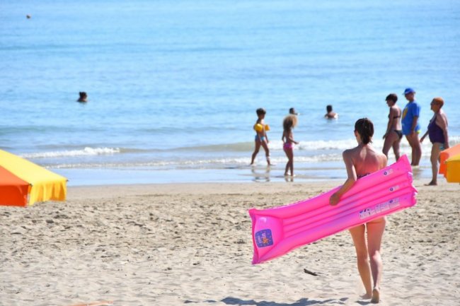 Persona sulla spiaggia con materassino rosa.
