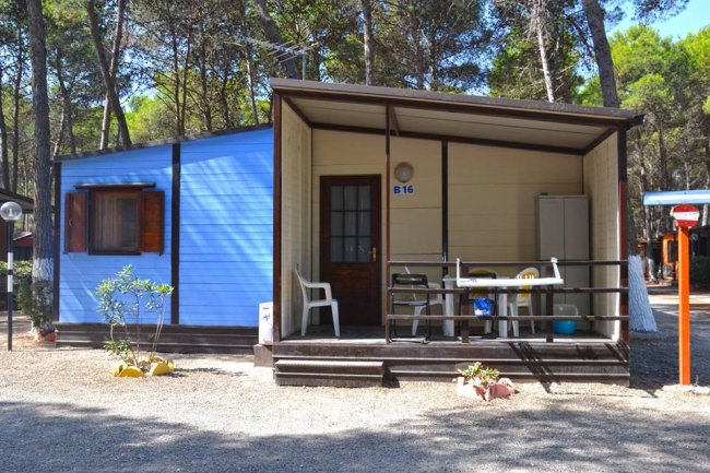 Casetta blu con veranda, sedie bianche e tavolo.
