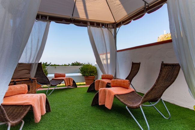 Gazebo con lettini di vimini e teli arancioni su un prato verde.