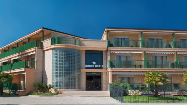Facciata di un hotel con balconi verdi, grandi finestre e un'insegna al centro.