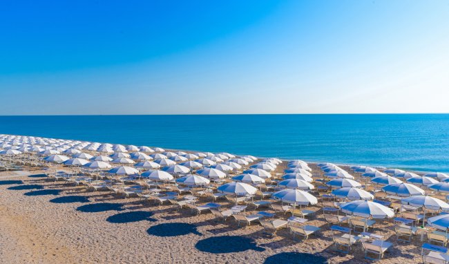 Spiaggia con file ordinate di ombrelloni bianchi e il mare azzurro sullo sfondo.