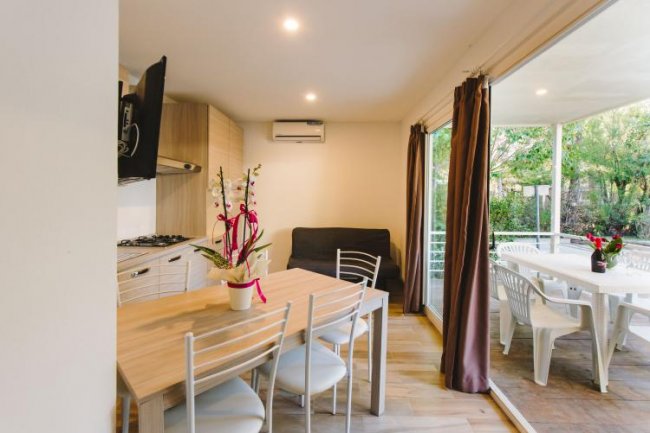 Interno moderno con tavolo da pranzo, cucina e porte finestre aperte su terrazza.
