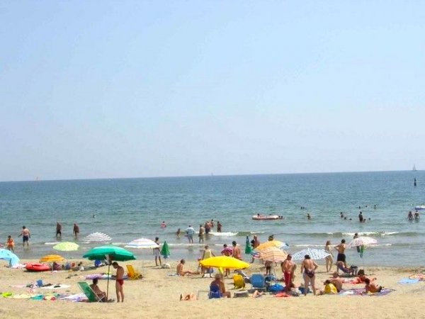 Spiaggia affollata con bagnanti e ombrelloni colorati davanti al mare.