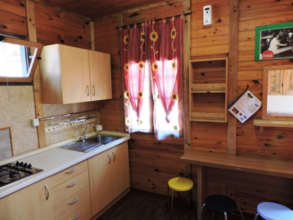Cucina in legno con pensili beige, lavello, fornelli e sgabelli colorati. Finestra con tende rosse.