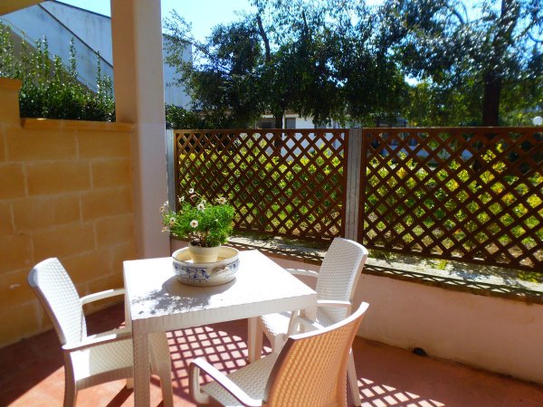 Terrazza con tavolo e sedie bianchi, pianta in vaso, luce solare.