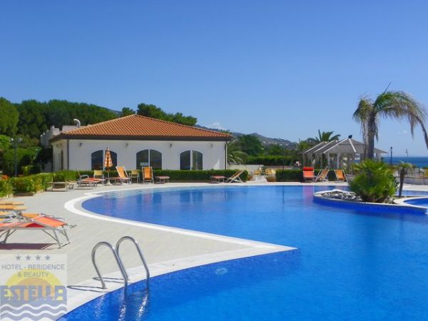 Piscina con sdraio e un edificio bianco, vista mare e cielo sereno.