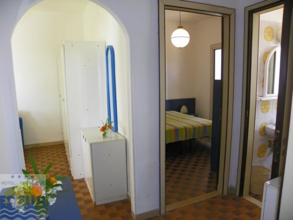 Corridoio di un hotel con letto a righe, armadio e bagno a vista.
