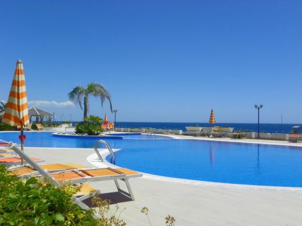 Piscina con lettini, ombrelloni a strisce e vista mare.